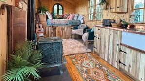 A cozy cabin interior with a wooden ceiling, a fireplace, a sofa set, and a kitchen area.