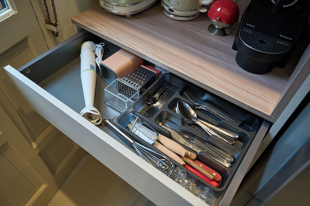 A kitchen drawer with utensils, a grater, and a coffee maker.
