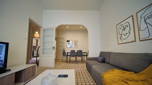 En moderne stue med en grå sofa, et sofabord med en glasfigur, et fjernsyn og et spiseområde med stole og bord.