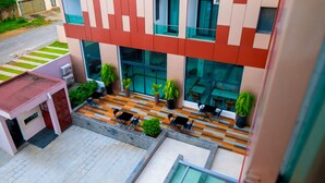Un edificio moderno con tejado plano, zona de estar exterior con mesas y sillas, y plantas en macetas.