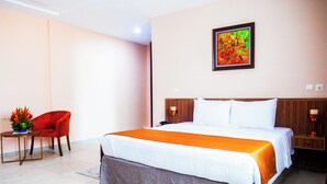 Habitación de hotel con una cama grande, una silla roja, una mesita con un jarrón y un cuadro en la pared.