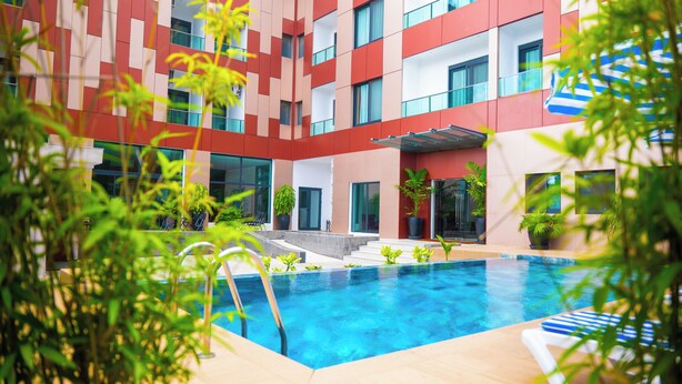 Un hotel moderno con piscina, mobiliario exterior y plantas en macetas.