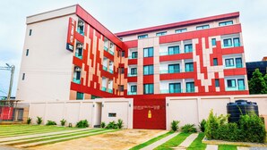 Un hotel moderno con fachada roja y blanca, varios balcones y una entrada con portón.