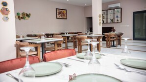 Un restaurante con varias mesas dispuestas para comer, sillas y una estantería de vinos en la pared.