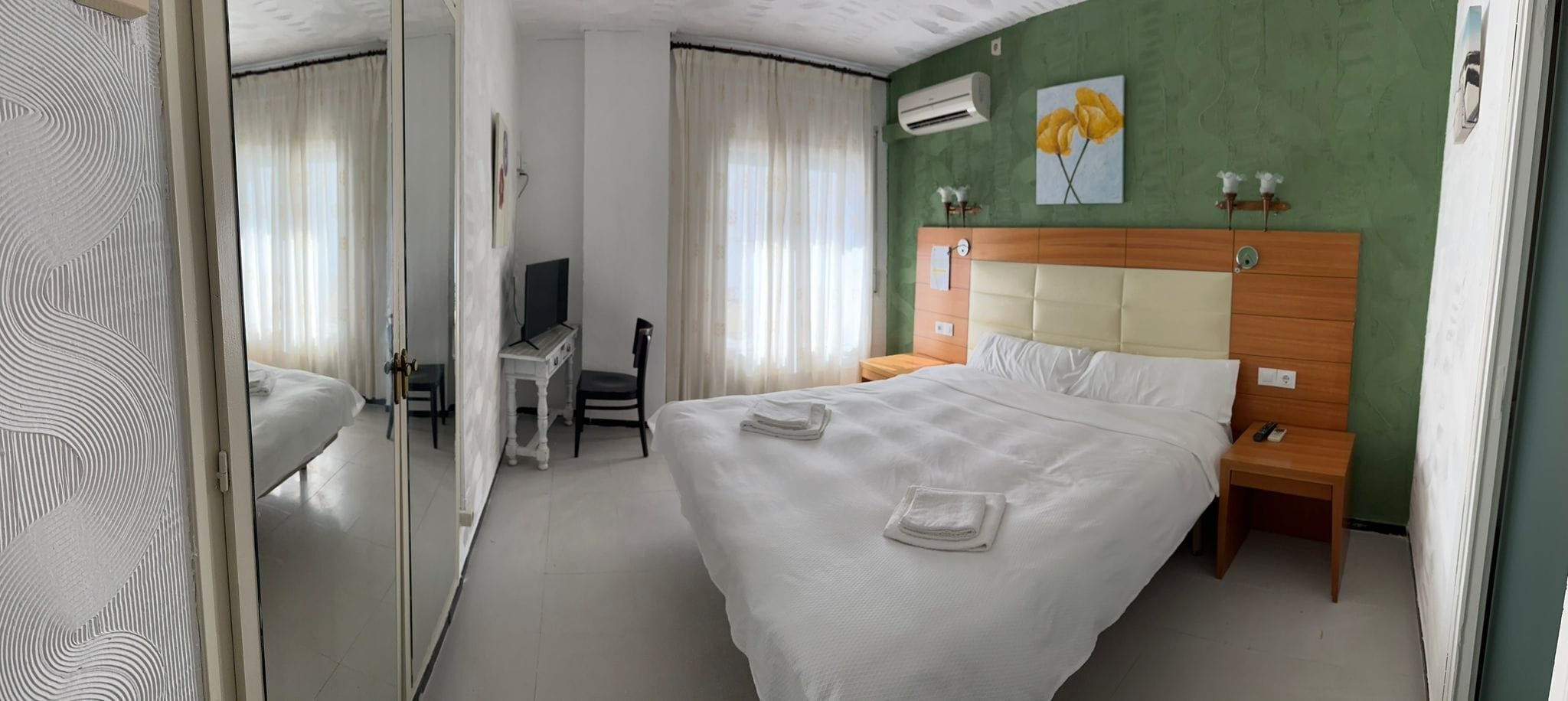 Habitación de hotel con cama, mesita de noche, televisión y una pared verde decorativa.