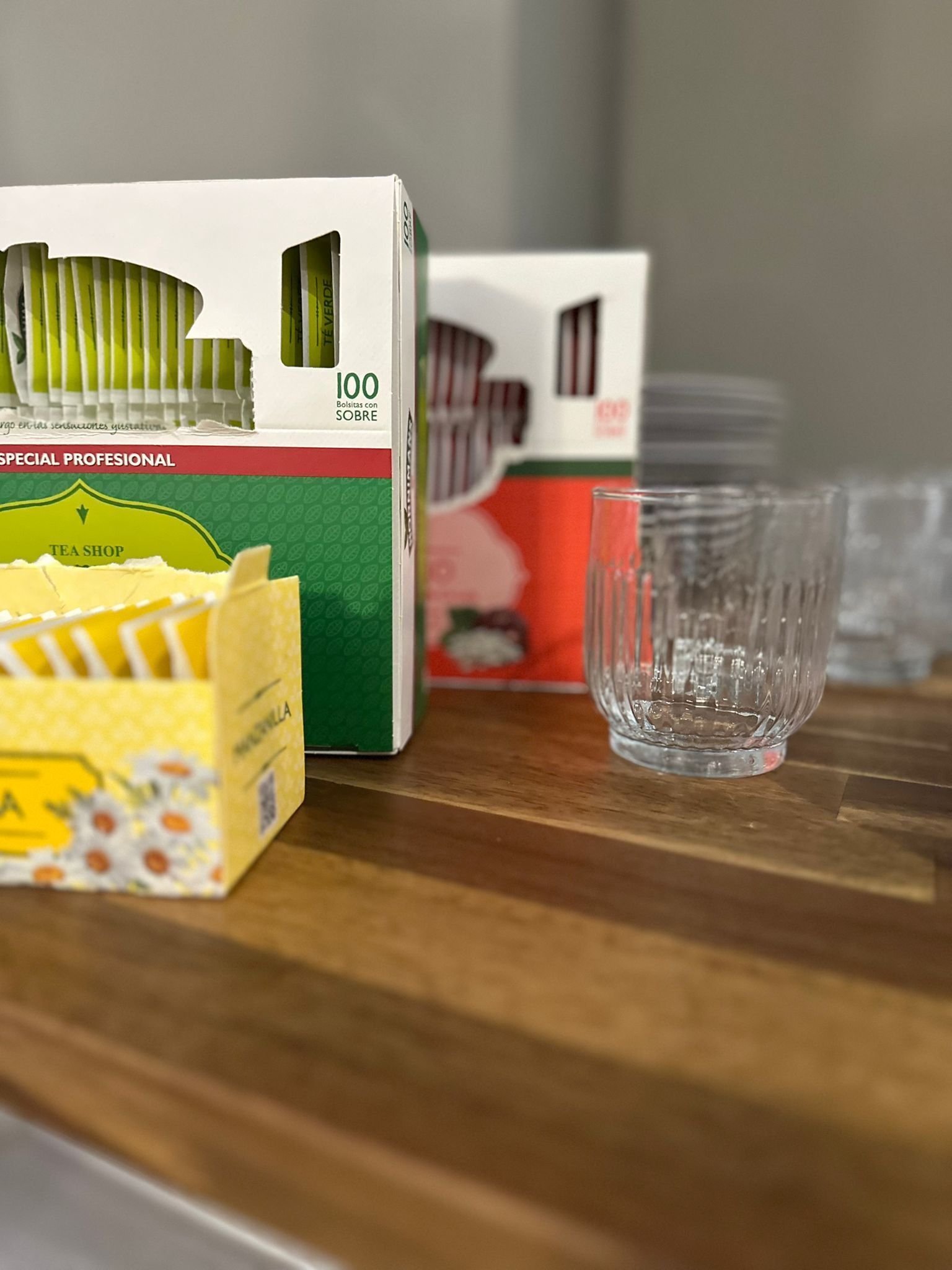 Een doosje theezakjes en een glas op een houten ondergrond.