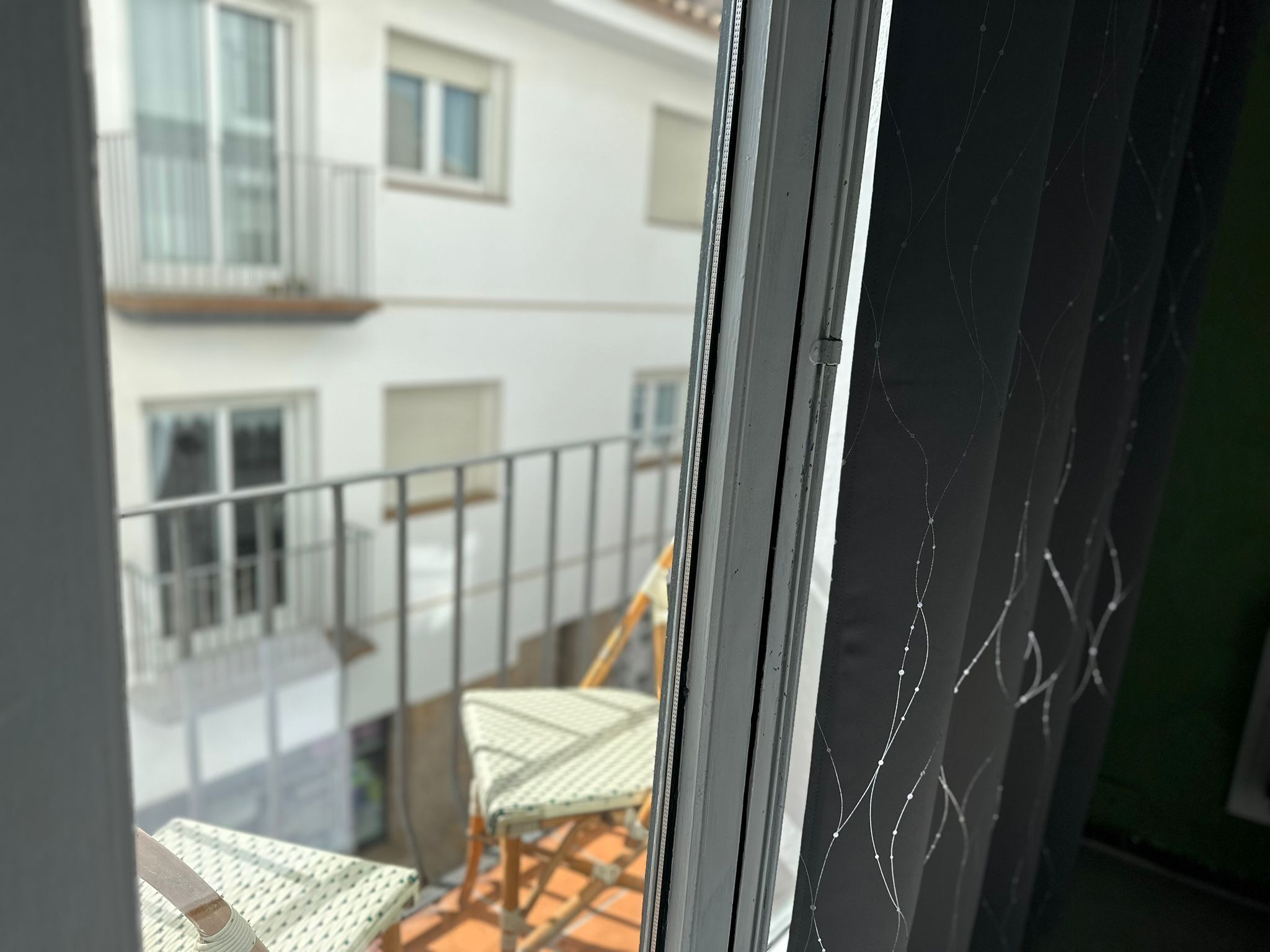 Een balkon met rieten meubilair, een leuning en uitzicht op een gebouw met ramen en balkons.