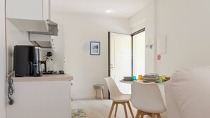 Une cuisine compacte équipée d’une machine à café, d’un petit réfrigérateur et d’un coin repas avec une table et des chaises.