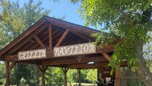 A wooden pavilion with a sign reading "GRILLIN PAVILION" and picnic tables underneath. - The Woods Lodging (Madill)