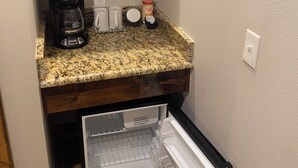 A compact kitchen with a microwave, coffee maker, and a refrigerator. - The Woods Lodging (Madill)