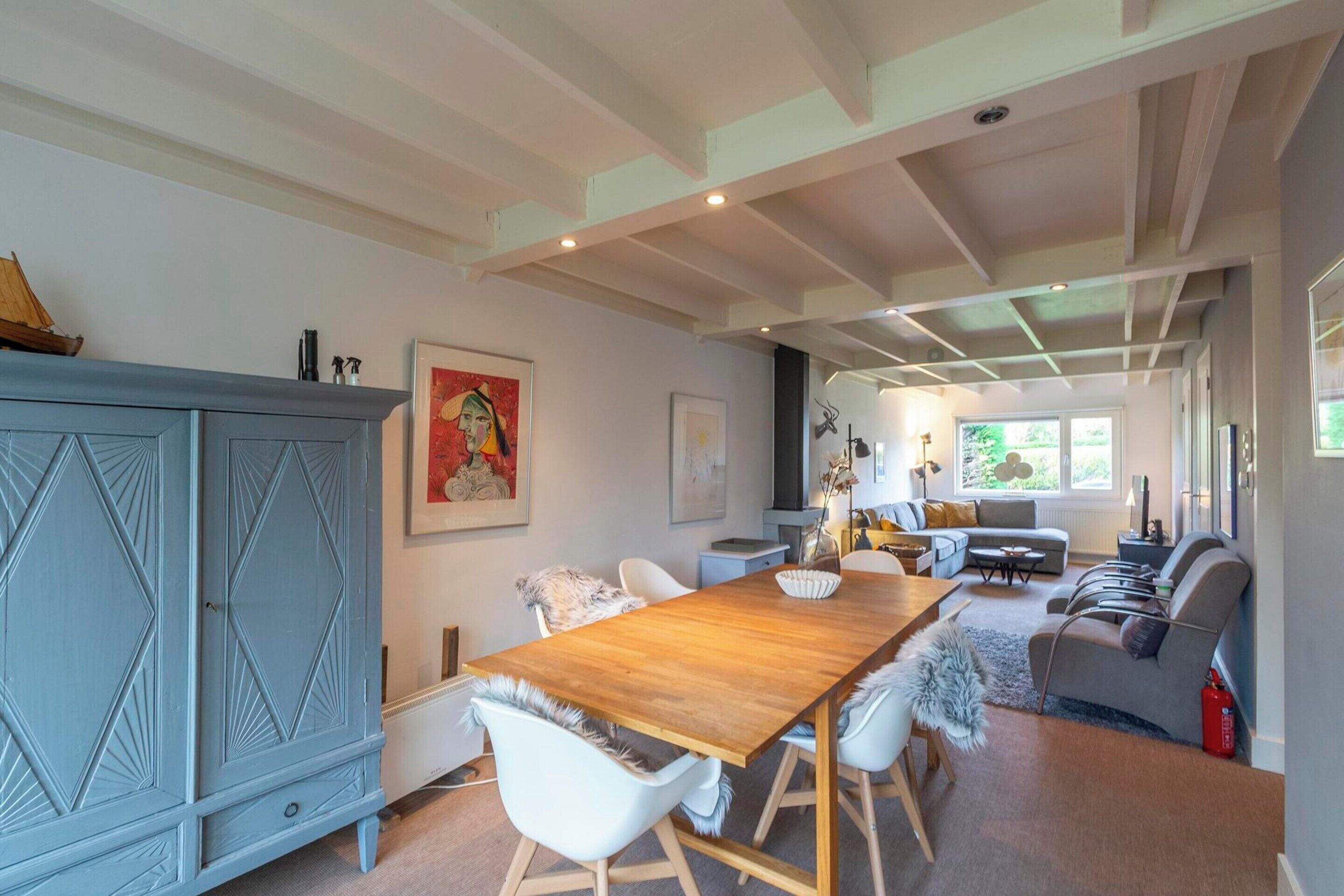 A spacious room with a wooden dining table, white chairs, a grey sofa, and a blue cabinet.
