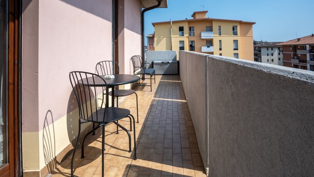 A balcony with a table and chairs, a suitcase, and a view of surrounding buildings. - Apartment with garage near the center of Verona (Verona)