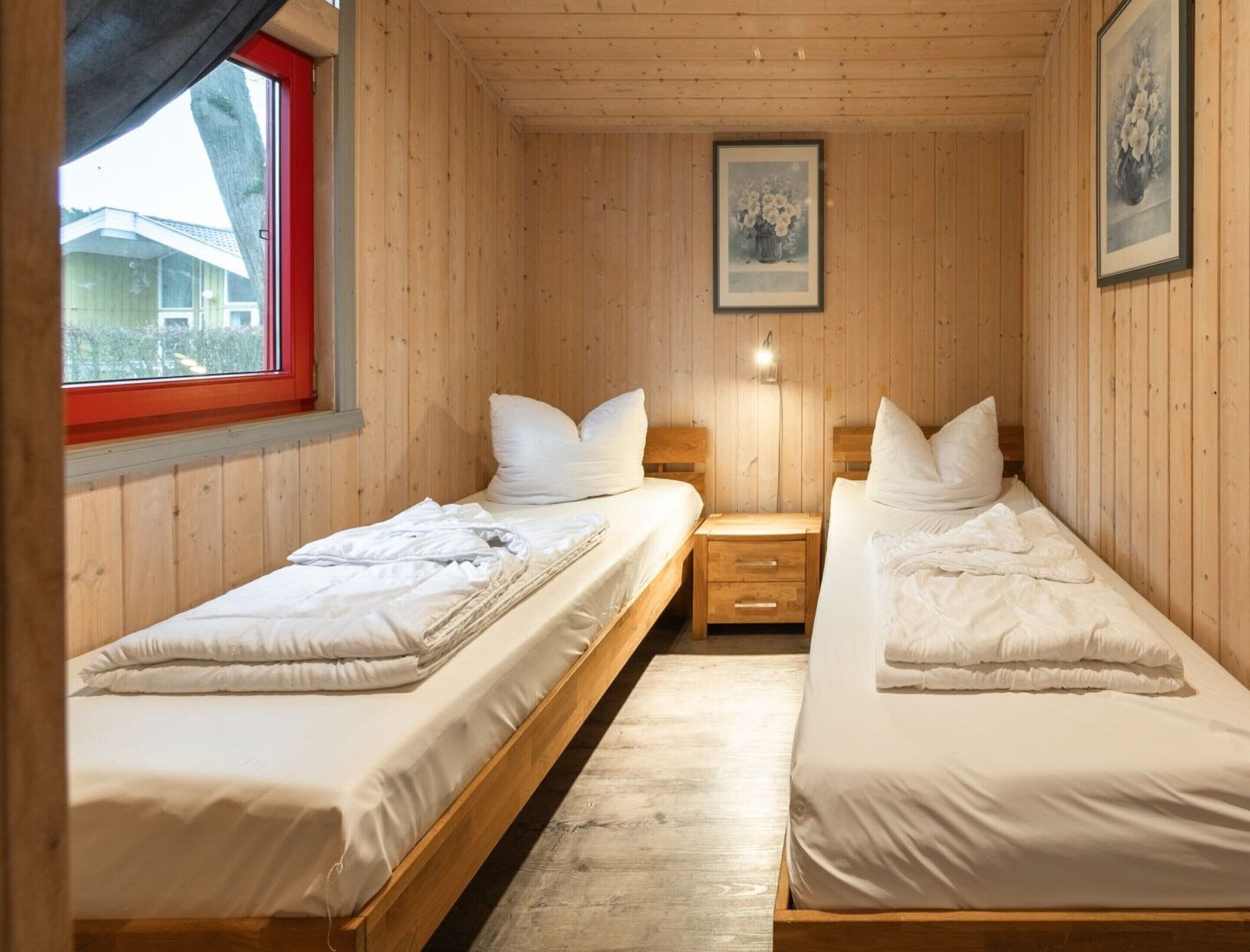 Une chambre dans une cabane en bois, avec deux lits, une fenêtre et un tableau encadré au mur.
