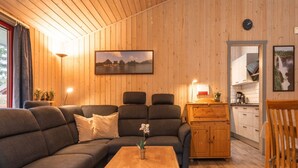 Een gezellige woonkamer met een hoekbank, een houten salontafel en een keukenhoek met kastjes en een spoelbak.