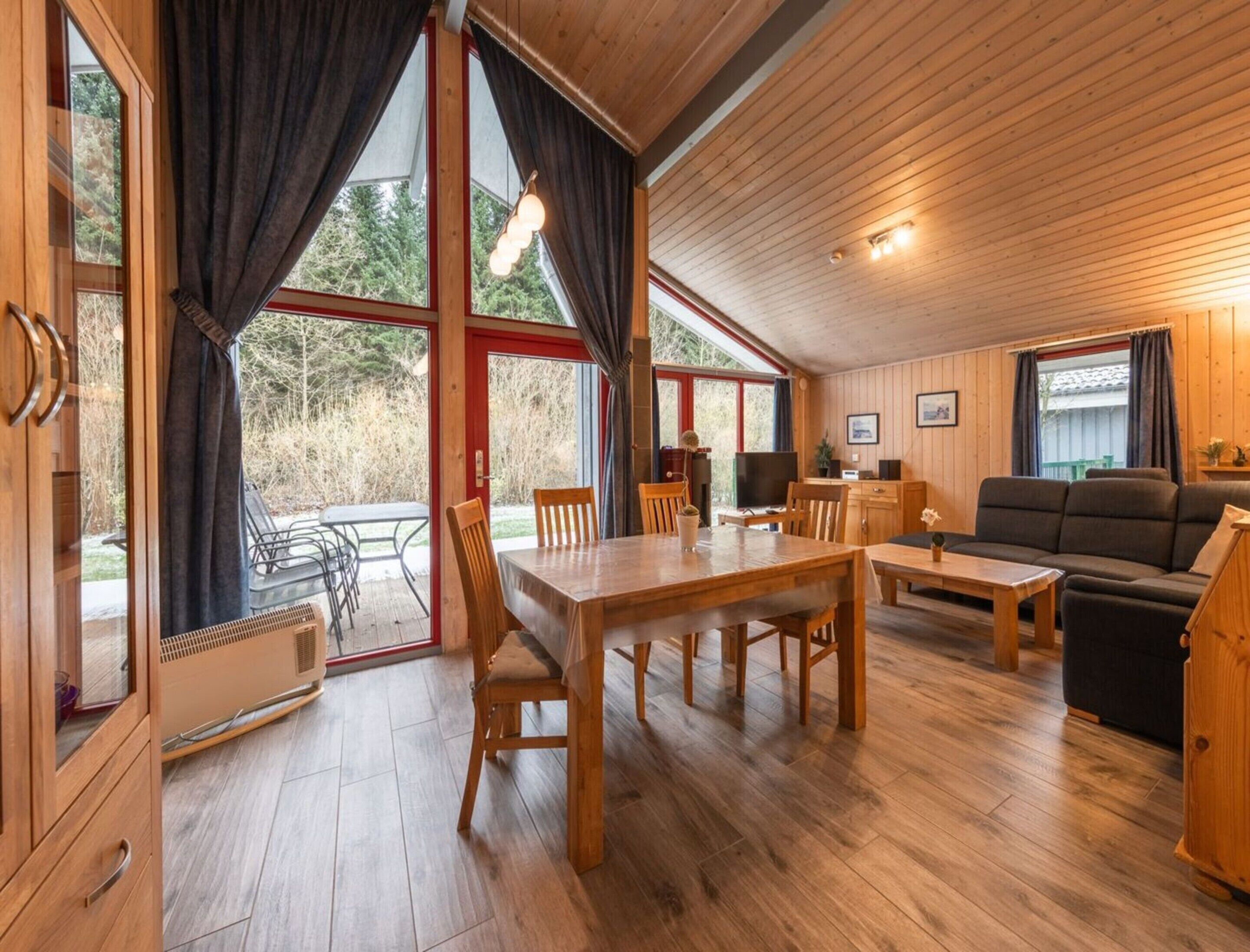 Ein gemütliches Blockhaus-Interieur mit Essbereich, einer Couch und einem großen Fenster mit Blick auf einen bewaldeten Bereich.