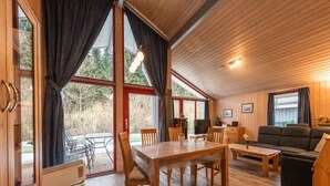 Een gezellig cabin interieur met een eethoek, een bank en een groot raam met uitzicht op een bebost gebied.