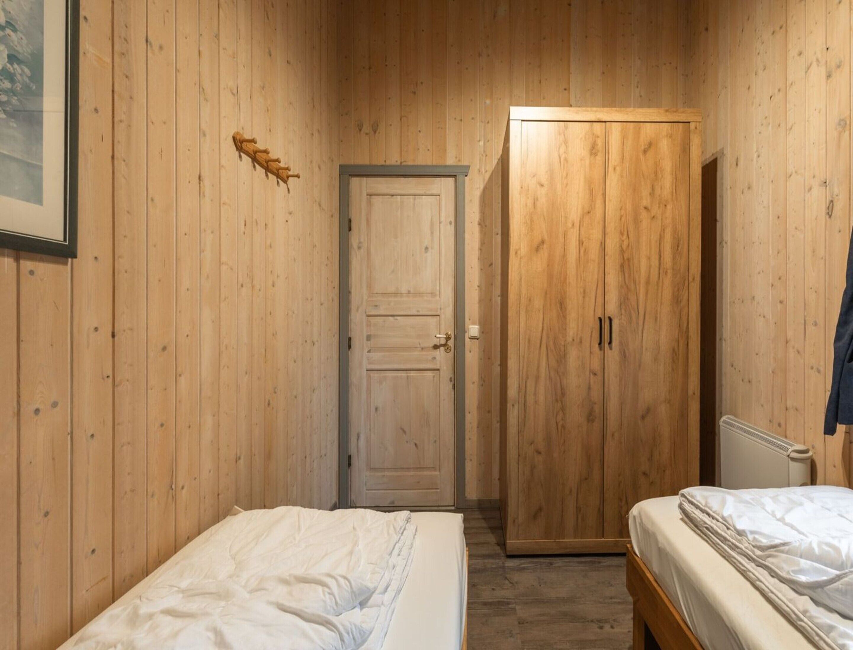 Ein kleiner Raum mit Holzvertäfelung, zwei Betten, einem Kleiderschrank und einer Heizung.