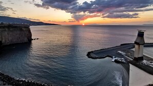 Vista de un atardecer costero con un faro y un litoral rocoso.
