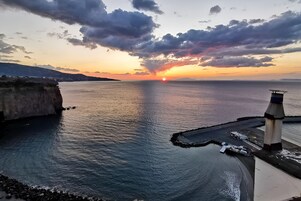 Vista de un atardecer costero con un faro y un litoral rocoso.