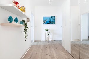 Un pasillo moderno y minimalista con suelo de madera, paredes blancas y un cuadro enmarcado de un paisaje.