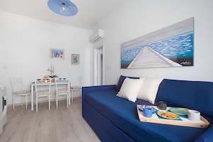 Una habitación moderna con un sofá azul, una mesa de comedor con sillas y un cuadro en la pared.