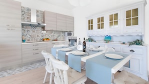 A modern kitchen with white cabinets, a tiled backsplash, and a dining area set for six with blue tablecloths and white chairs.