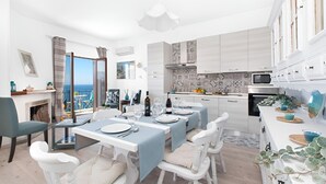 A modern dining area with a view of the sea, a kitchen with white cabinets, and a dining table set with plates and glasses.