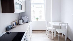 Une cuisine lumineuse avec des meubles blancs, une cuisinière, un four à micro-ondes et une fenêtre donnant sur des immeubles.