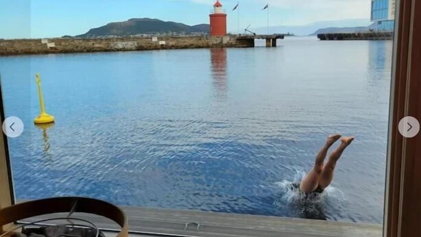 Une vue prise depuis un bateau, montrant une personne qui plonge dans l’eau, un phare et une mer calme.