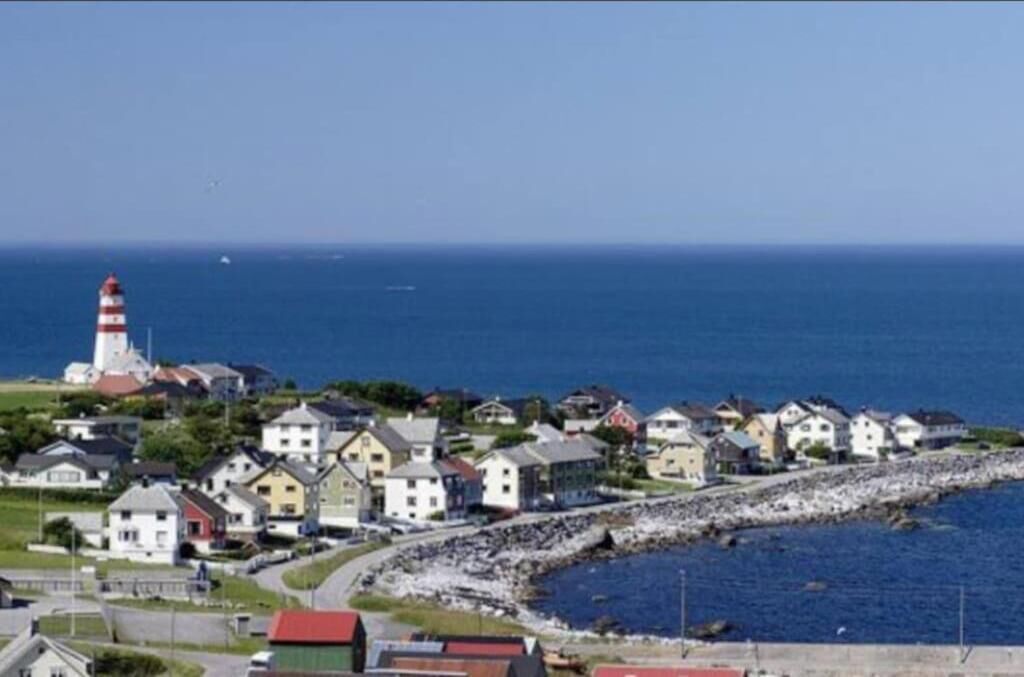 A coastal town with a lighthouse, houses along the shore, and a rocky breakwater.