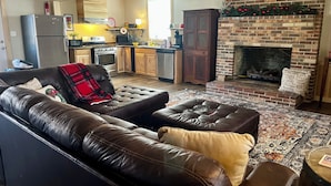 A living room with a leather sofa, a fireplace, and a kitchen in the background. - Cozy 2-bedroom cabin in charming Lexington with WiFi, AC (Lexington)