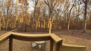 A wooden deck with a metal chair and a table, surrounded by a forest with leafless trees. - Cozy 2-bedroom cabin in charming Lexington with WiFi, AC (Lexington)
