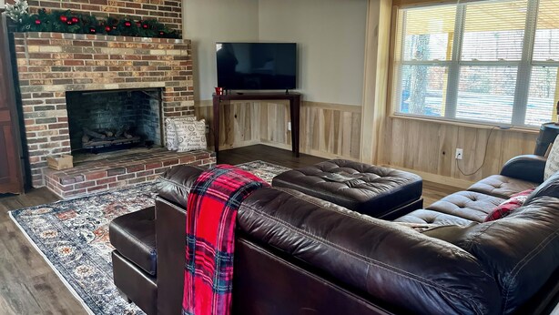 A living room with a brick fireplace, leather sofas, a flat-screen TV, and a large window with blinds. - Cozy 2-bedroom cabin in charming Lexington with WiFi, AC (Lexington)