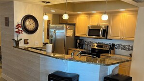 Cocina moderna con una isla central, electrodomésticos de acero inoxidable e iluminación colgante.