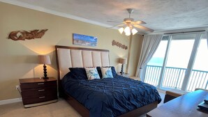 Un dormitorio con una cama grande, un escritorio, un ventilador de techo y vistas al exterior.