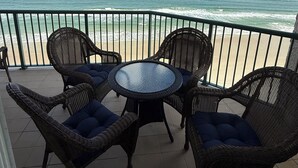 Un balcón con mobiliario de mimbre y una mesa de vidrio con vista a la playa y al océano.