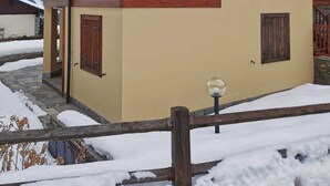 A two-story wooden chalet with a balcony, a stone foundation, and a snowy landscape in the background. - [Cogne - Gran Paradiso] Chalet La Grivola (Gimillan)