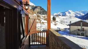 A wooden balcony with a stone wall, a wooden door, and a view of snow-covered mountains. - [Cogne - Gran Paradiso] Chalet La Grivola (Gimillan)