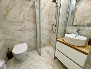 A modern bathroom with a glass-enclosed shower, a white toilet, and a wooden vanity with a sink.