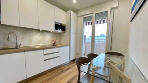 A modern kitchen with white cabinets, a stainless steel sink, and a glass dining table with two chairs. - Renovated Apartment With Balcony (Caorle)