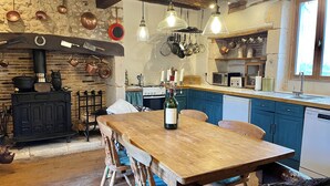 Una cocina rústica con una mesa de madera, ollas colgantes y una estufa negra.