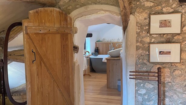 Un interior rústico con una puerta de madera, paredes de piedra y un baño con lavamanos y bañera.