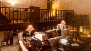 Una habitación acogedora con pared de piedra, escalera de madera, sofá, mesa y dos lámparas.