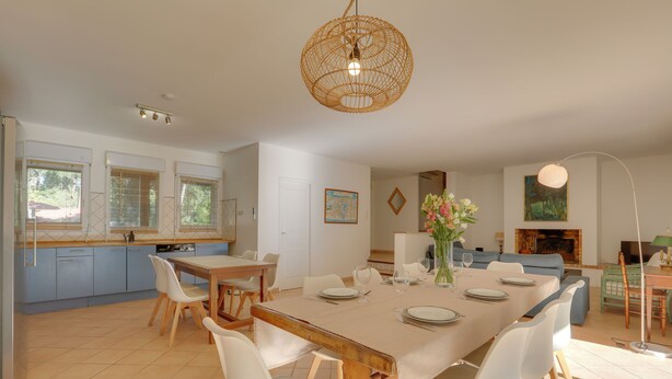 Un comedor espacioso con una gran mesa de madera, sillas blancas y una lámpara colgante.