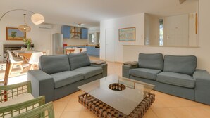 Una sala de estar moderna con dos sofás grises, una mesa de centro de vidrio y un comedor con una mesa y sillas de madera.