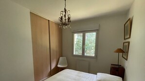 Un dormitorio con cama, candelabro, ventana, silla y mesita de noche.