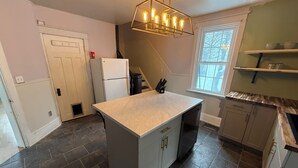 A kitchen with a central island, dark tiled flooring, a refrigerator, a dishwasher, and a window with a view.