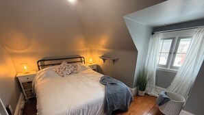 A bedroom with a bed, two bedside tables with lamps, a window with curtains, and a potted plant.