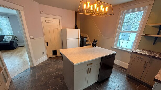 A kitchen with a central island, dark tiled flooring, a refrigerator, a dishwasher, and a window with a view.