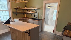 A kitchen with a central island, wooden shelves above, and a view to the outside.